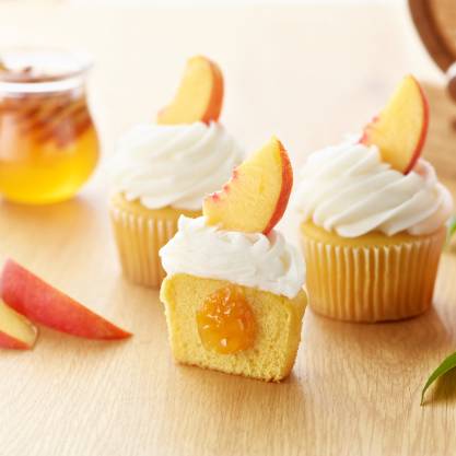 Peach-filled cupcakes topped with whipped frosting and fresh peach slices, featuring a juicy peach filling center.