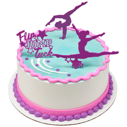 Round cake with blue icing and pink accents topped with purple gymnast cake picks and a Flip Jump Tuck sign.