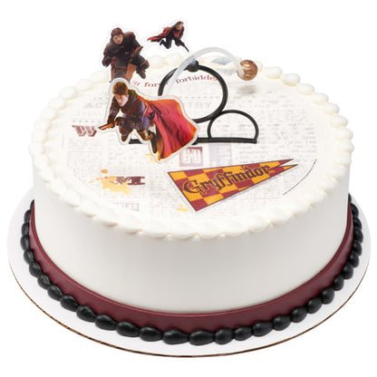 A round cake with a newspaper-themed edible image, bordered in white and maroon frosting, topped with the Harry Potter™ Quidditch DecoSet.