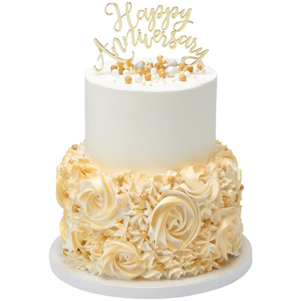 Gold Happy Anniversary cake topper displayed on a two-tiered cake with cream-colored floral decorations and pearl accents.