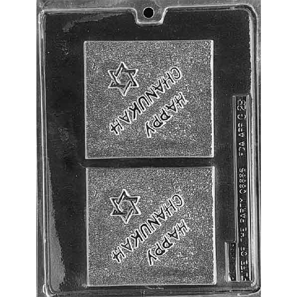 Clear plastic chocolate mold with two large square cavities embossed with the words “Happy Chanukah” and a Star of David, shown on a dark background.