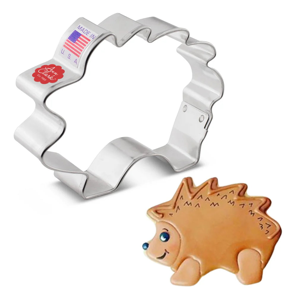 Hedgehog-shaped metal cookie cutter alongside a decorated hedgehog-shaped cookie with a cute face and spiky details.