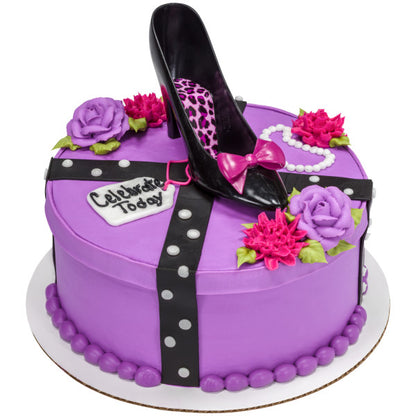 Round purple cake with black high heel topper, floral accents, and fondant decorations including a “Celebrate Today” tag.