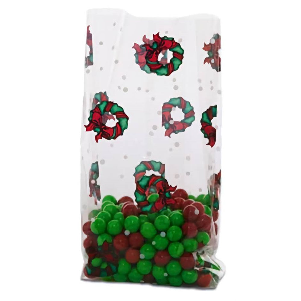 A medium-sized cellophane treat bag filled with red and green candies, reminiscent of holiday colors. The bag is adorned with a pattern of festive wreaths that feature red bows, set against a clear background dotted with white snowflakes. This holiday wreath design adds a traditional Christmas touch, making it ideal for seasonal gifts or treats.