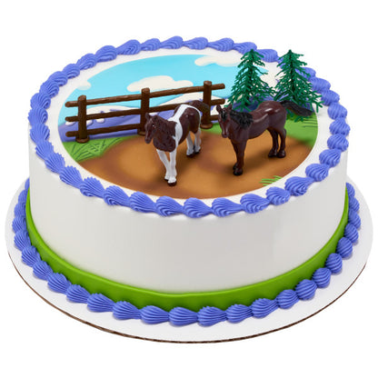 Round cake with horses cake topper set on an icing pasture with blue sky and fence.