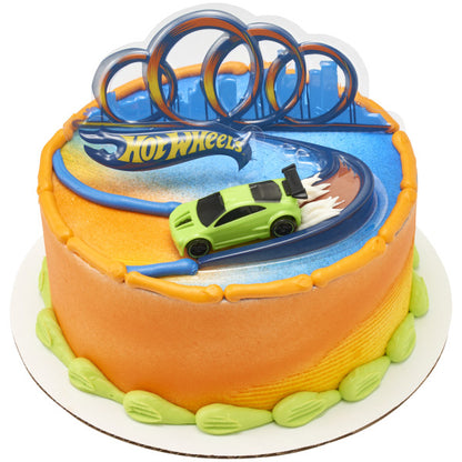 A racing-themed round cake decorated with a Hot Wheels car speeding down a curved track with a triple-loop backdrop.