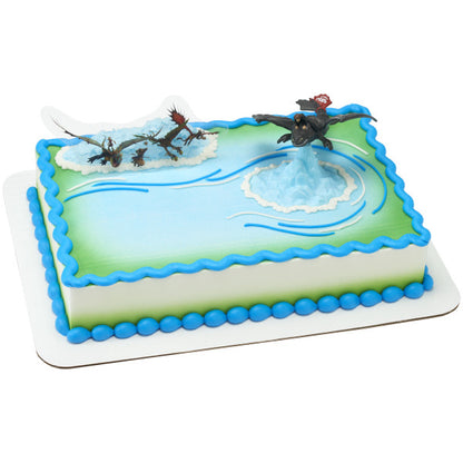 Rectangular cake with green and blue icing, topped with Toothless pivoting figurine and dragon background pick.