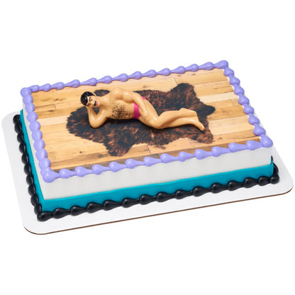 A rectangular cake decorated with a faux wooden floor and fur rug, featuring the Hunky Man figurine.