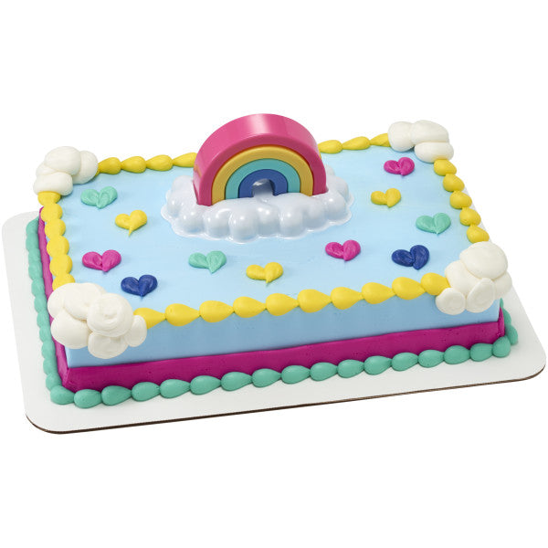 Rectangular sheet cake with light blue icing, yellow piped border, pastel heart decorations, and a rainbow topper on a white cloud tray centered on top.