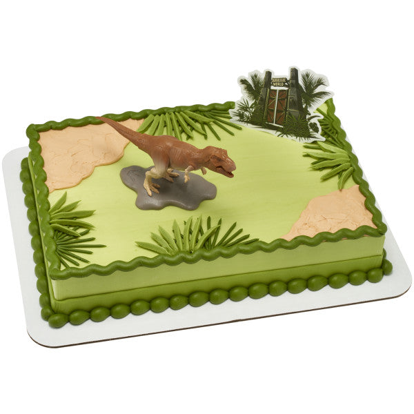 A rectangular cake decorated with green jungle scenery, a roaring T-Rex cake topper, and the iconic Jurassic World™ gate.