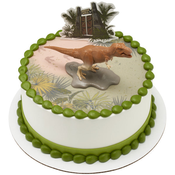 A round cake featuring a printed prehistoric landscape, a T-Rex figurine, and the Jurassic World™ gate as a backdrop.