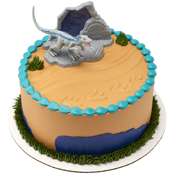 A round cake featuring a prehistoric desert design with Blue Raptor standing on a rock and a Jurassic World™ backdrop.
