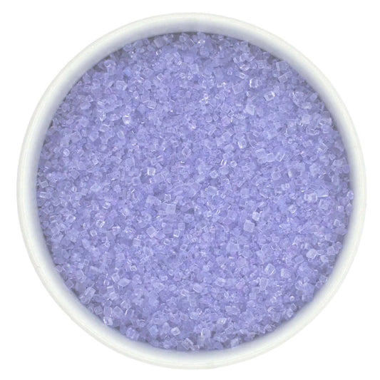 Top-down view of a white bowl filled with lavender coarse sanding sugar crystals, showing pale purple, chunky granules with a clear sparkling shine.