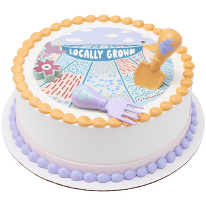 A farm-inspired cake with a "Locally Grown" design, featuring the toy fork, shovel, and flower candle holder.