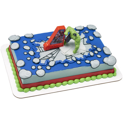 Rectangular Avengers-themed cake with blue top, web-style lines and gray icing dots, topped with Hulk figure and red Avengers sign centerpiece.