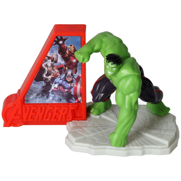 Hulk cake topper with green Hulk figure on a gray textured base next to a red Avengers sign featuring Marvel characters, photographed on a white background.