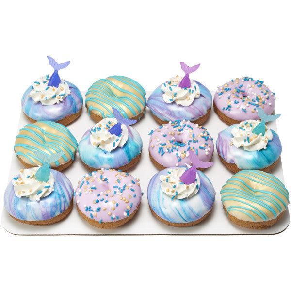 Assorted donuts decorated with blue, purple, and teal glazes, whipped topping, sprinkles, and colorful mermaid tail picks.