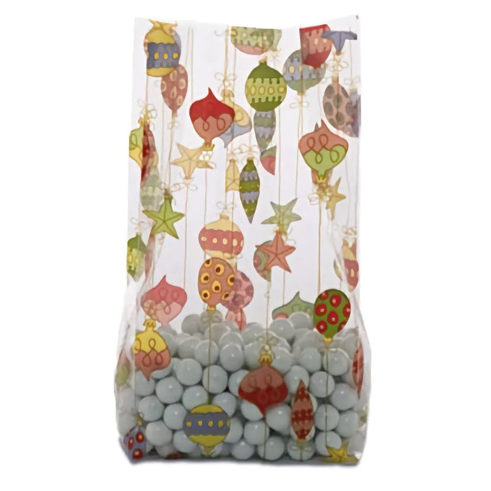 A festive medium-sized cellophane treat bag filled with pale blue candies. The bag features colorful Christmas ornaments in various shapes and patterns, suspended from golden strings against a clear background. The ornaments are decorated in shades of red, yellow, green, and more, creating a vibrant and cheerful holiday design.