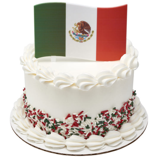 White frosted cake decorated with red, white, and green sprinkles, topped with a plastic Mexican flag cake topper.