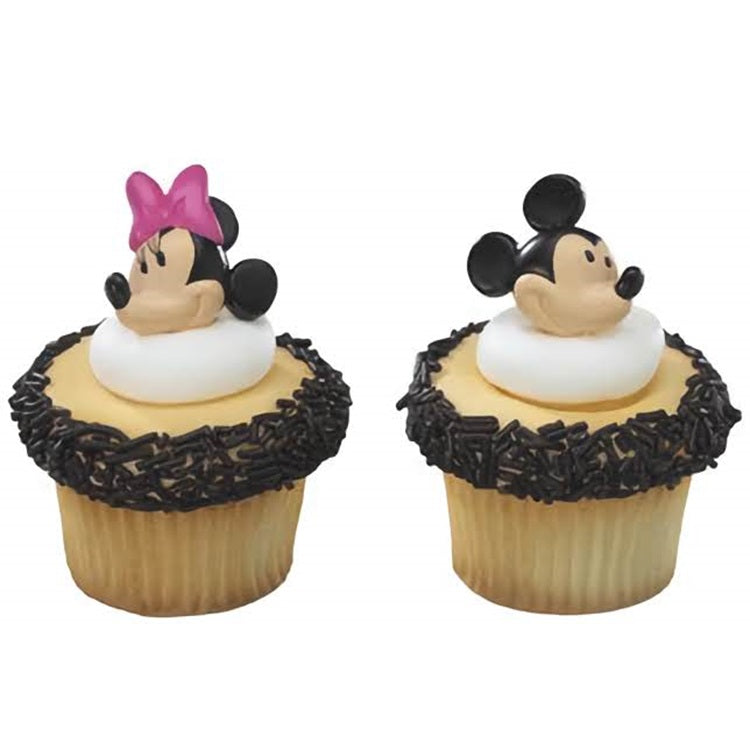 Frosted vanilla cupcakes with whimsical cupcake rings; one ring features mickey mouse and Minnie Mouse with a pink bow, both nestled atop creamy white icing and encircled by dark chocolate sprinkles.