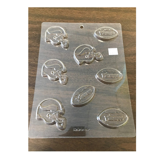 A clear plastic chocolate mold featuring football and helmet shapes, each embossed with the word 'Vikings,' indicative of the Minnesota Vikings team. The mold contains multiple cavities perfect for creating themed chocolates for sports events, game day parties, or as treats for fans of the football team.