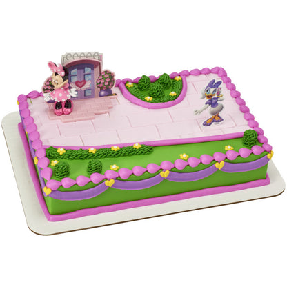 Rectangular cake decorated with Minnie Mouse and Daisy Duck figures, pink and green icing, and heart-shaped details.