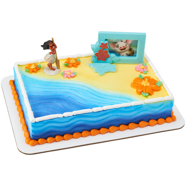 A beach-themed rectangular cake with blue ocean waves, sandy shores, tropical flowers, and the Moana topper set.