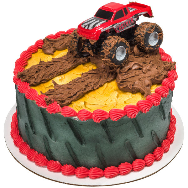 A round cake decorated with tire tread patterns and muddy frosting, featuring the Crusher monster truck topper.