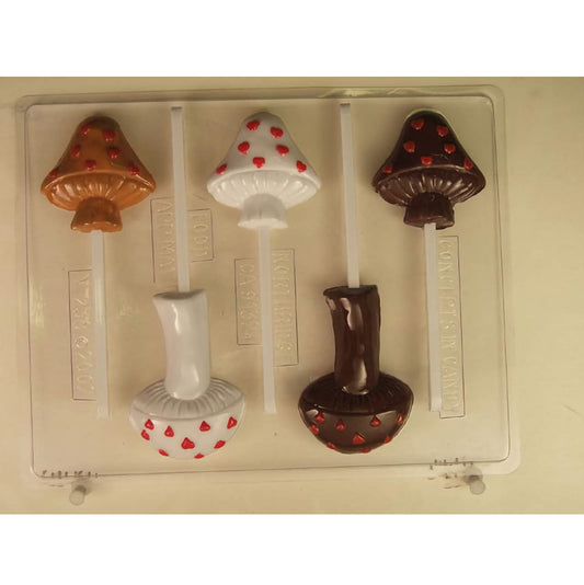 Chocolate sucker mold featuring various styles of mushrooms and toadstools. The clear mold has cavities for two different designs, including classic mushroom shapes and whimsical toadstools with heart-shaped spots. The chocolates are displayed as finished products, with colorful details and sticks attached, indicating the mold's use for making fun and creative lollipop treats.