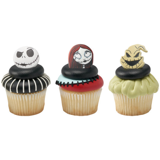 Three cupcakes topped with Nightmare Before Christmas character rings, featuring Jack Skellington, Sally, and Oogie Boogie on black, red, and green themed frosting designs.
