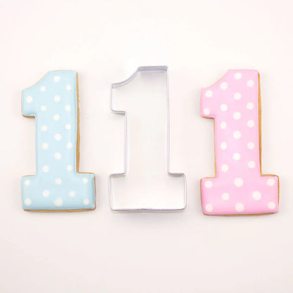 Number one cookie cutter alongside blue and pink polka dot cookies, ideal for birthdays or special events.