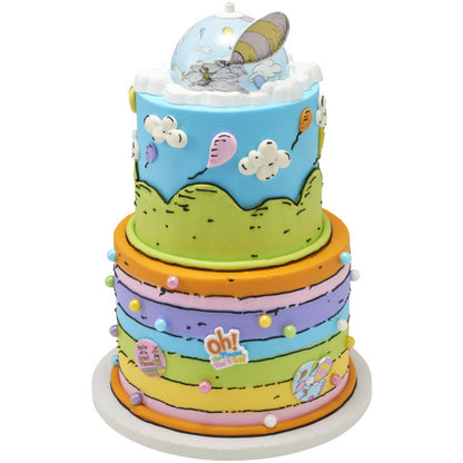 A colorful, multi-tiered cake with stripes, hills, and clouds, topped with the spinning dome decoration.