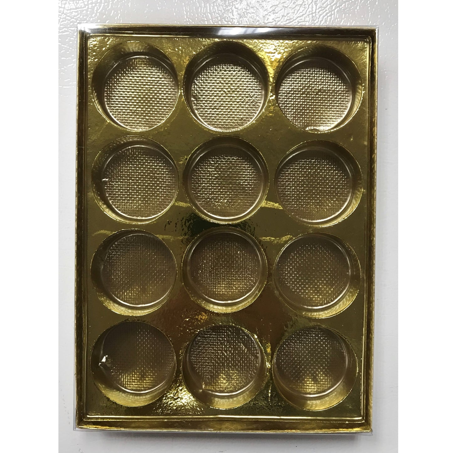 The photo shows a gold candy box insert with twelve round, textured cavities for holding individual chocolates or truffles.