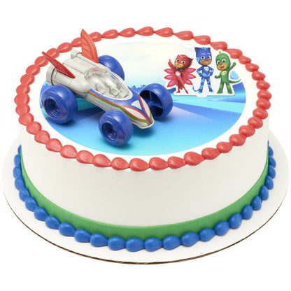 A round cake decorated with the PJ Masks Saves the Day DecoSet®, with the Cat-Car and character topper placed on a PJ Masks-themed edible image.