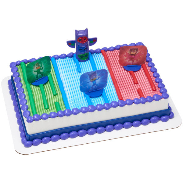 A rectangular cake decorated with the PJ Masks We're on Our Way DecoSet®, featuring the transformation totem pole and character stands on a colorful striped background.