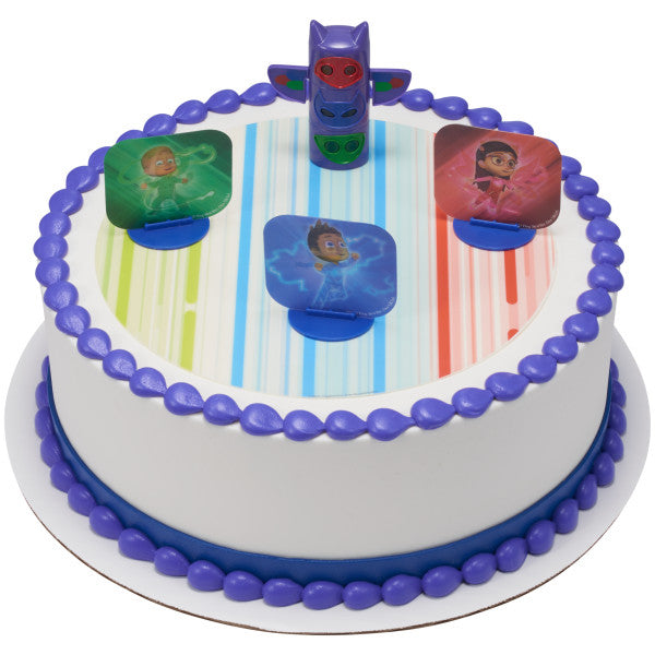 A round cake decorated with the PJ Masks We're on Our Way DecoSet®, with the transformation totem pole and character stands placed on a matching edible image.