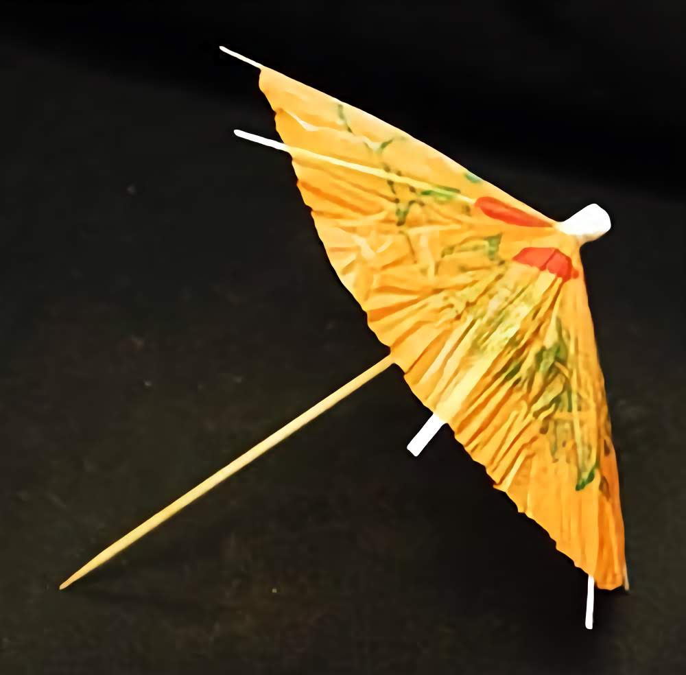 Orange paper umbrella cupcake topper pick with a floral design, displayed against a dark background.