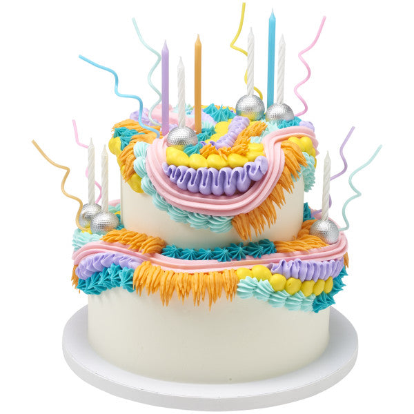 Two-tier white cake decorated with colorful piped buttercream in teal, orange, pink, and purple, topped with pastel twist shaped candles, silver disco ball decorations, and white striped candles.