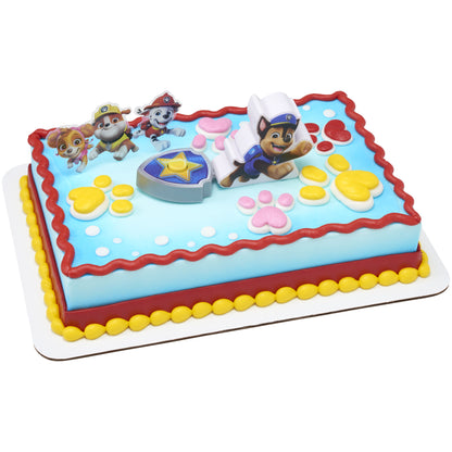 PAW Patrol Adventure Bay Heroes cake decorated with Chase launcher, shield badge, and character pic featuring Skye, Rubble, Marshall, and Chase on blue frosting with colorful paw prints.