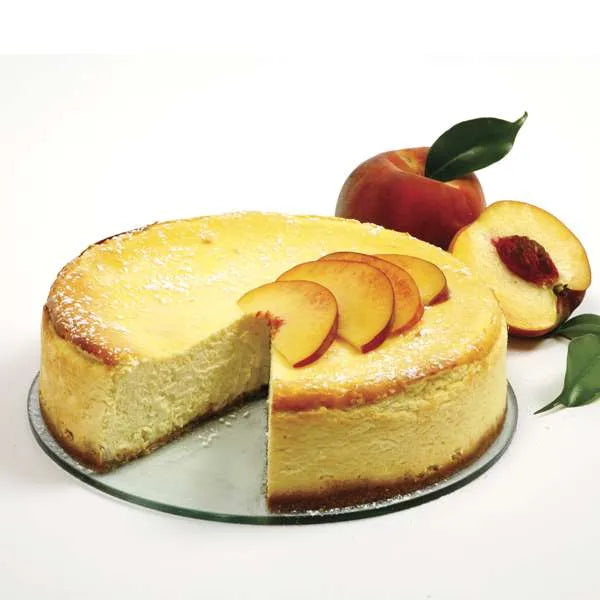 Baked cheesecake topped with peach slices, with whole and halved peaches in the background.