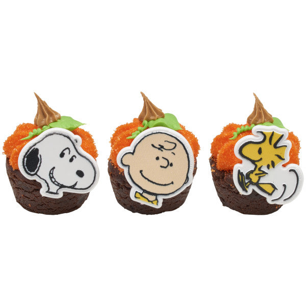 Three cupcakes decorated with orange and green frosting, topped with Peanuts rings featuring Snoopy, Charlie Brown, and Woodstock.