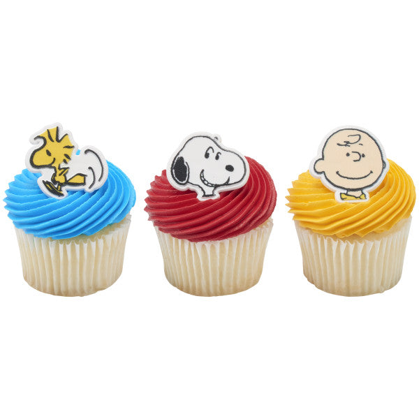 Three cupcakes topped with brightly colored frosting and Peanuts rings featuring Woodstock, Snoopy, and Charlie Brown.