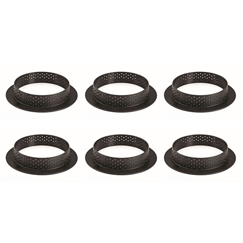 Six black perforated tart rings with flat bases, arranged in two rows on a white background, each ring featuring small holes around the sides for airflow during baking.