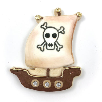 Pirate ship-shaped cookie decorated with a white sail featuring a skull and crossbones, and a brown ship with gold details.