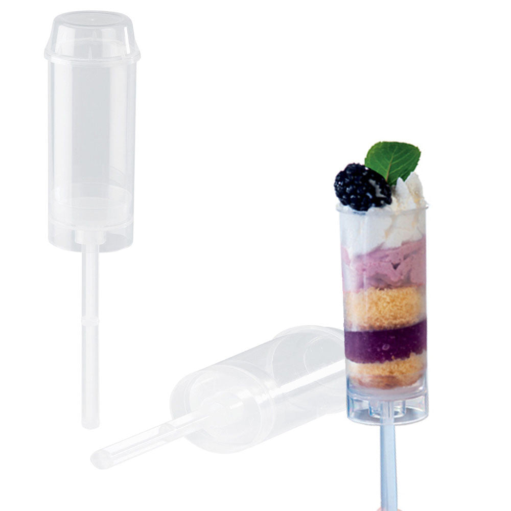 Clear mini push pop dessert cups with lids and long push-up stems, shown alongside a filled layered dessert push pop with purple and cream layers topped with whipped cream, a blackberry, and a green leaf.