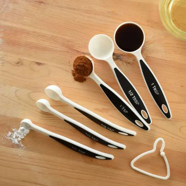 Overhead view of measuring spoons filled with spices and liquid ingredients on a wooden surface