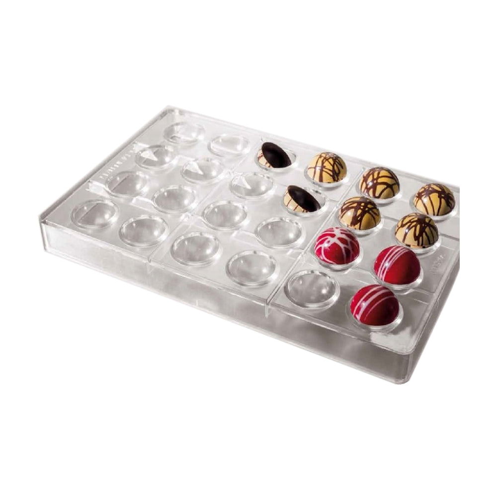 Clear polycarbonate chocolate mold with 24 hemisphere cavities; several finished domes are shown in gold with dark drizzle and red with white drizzle.