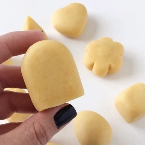 Hand holding a smooth, molded popsicle-shaped cake pop with other molded cake shapes in the background.