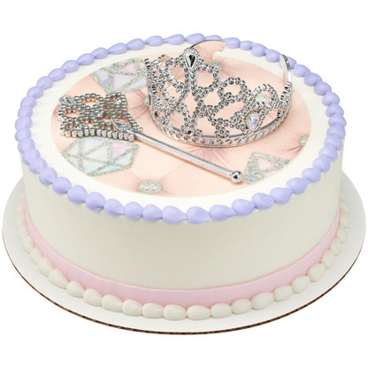 Round princess-themed cake topped with a tiara and wand on a pink background