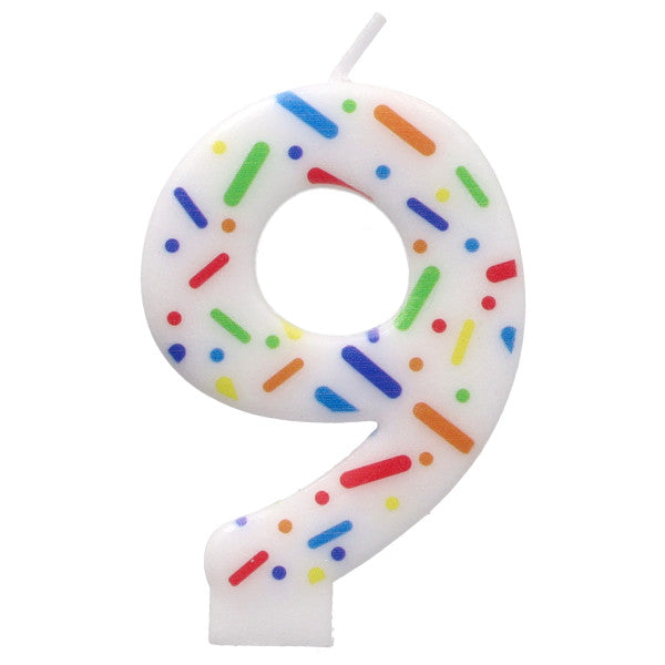 Candle shaped like the number 9 with colorful sprinkles on a white background